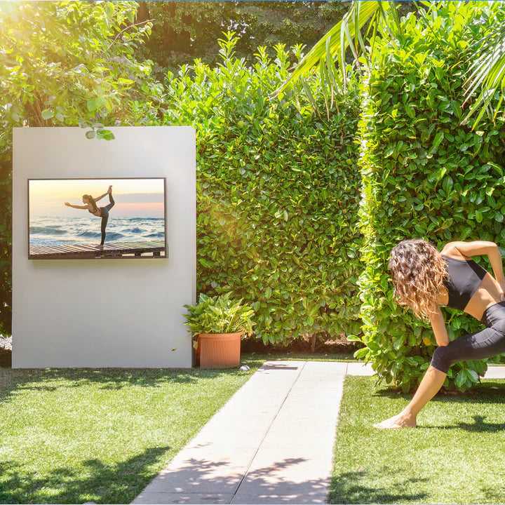Mädchen schaut sich Yoga-Videokurse auf einem intelligenten Outdoor-Fernseher im Sonnenschein auf dem Rasen an